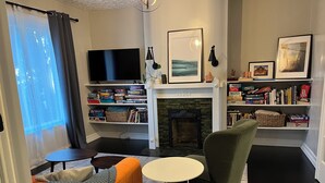 A living room with a fireplace, a television, a bookshelf, and a comfortable seating area. - Entire Apartment walking distance to Cincy River front and COV Wedding Venues (Covington)