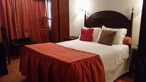 A neatly made bed with a red bedspread, white pillows, and a wooden headboard. - Guest House Casa dos Serpas (Nelas)