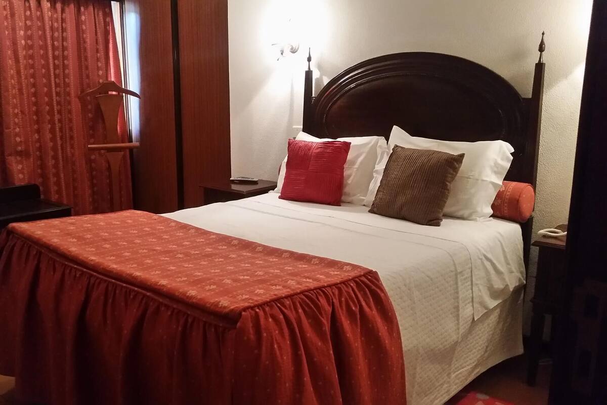 Un lit bien fait, avec une couverture rouge, des oreillers blancs et une tête de lit en bois.