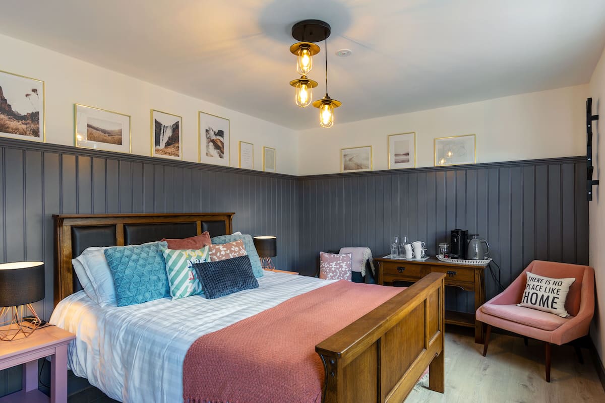 A bedroom with a bed, bedside tables, a chair, a desk, and framed pictures on the wall.