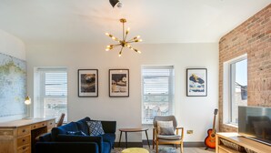 A modern living room with a blue sofa, a yellow ottoman, a wooden desk, and a TV on a wooden stand. - Macs Townhouse (Dungarvan)