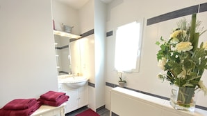 Un baño con un lavamanos blanco, espejo y un florero con flores en la pared.