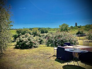 Een terras met een tafel en stoelen, omringd door een tuin met verschillende planten en bloemen.