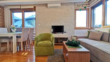 A modern living room with a stone wall, a flat-screen TV, a green armchair, a wooden coffee table, and a sofa.