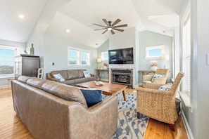 A spacious living room with a high ceiling, a fireplace, a television, and comfortable seating. - Corolla Odyssey: Dog-Friendly, Elevator, Hot Tub, Private Pool (Corolla)