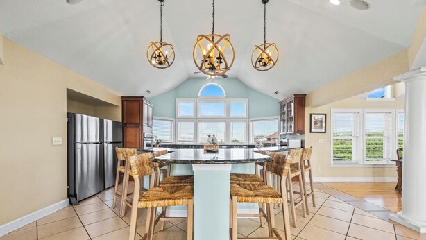 A spacious kitchen with a central island, modern appliances, and a dining area with wicker chairs. - Corolla Odyssey: Dog-Friendly, Elevator, Hot Tub, Private Pool (Corolla)
