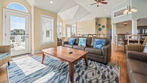 A spacious living room with a large sofa, a coffee table, and a dining area with chairs. - Corolla Odyssey: Dog-Friendly, Elevator, Hot Tub, Private Pool (Corolla)