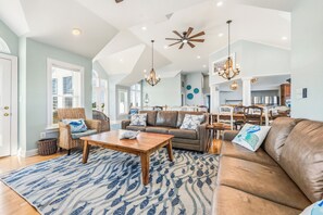Un salon spacieux avec un plafond haut, une table basse en bois placée au centre et un grand canapé en cuir marron.