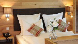 A hotel room with a wooden headboard, white bedding, two pillows, a bedside table with a lamp, a vase with flowers, and a phone on the nightstand. - Landgasthof Karolinenhöhe (Lichtenfels)