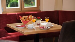 A breakfast setting with a wooden table, red upholstered booth seating, and a window with a view of greenery. - Landgasthof Karolinenhöhe (Lichtenfels)