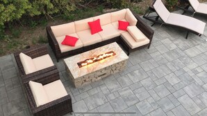 An outdoor seating area with a stone fire table and wicker furniture. - In-town 5 Bedroom Victorian With Heated Pool (Lubec)