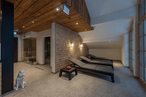 A modern spa area with wooden ceiling beams, a stone wall, and two lounge chairs.