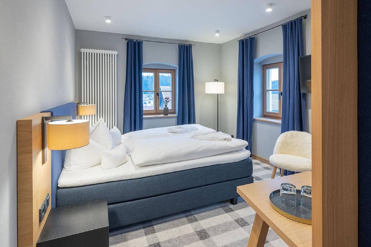 A hotel room with a bed, a chair, a table, and a window with curtains.