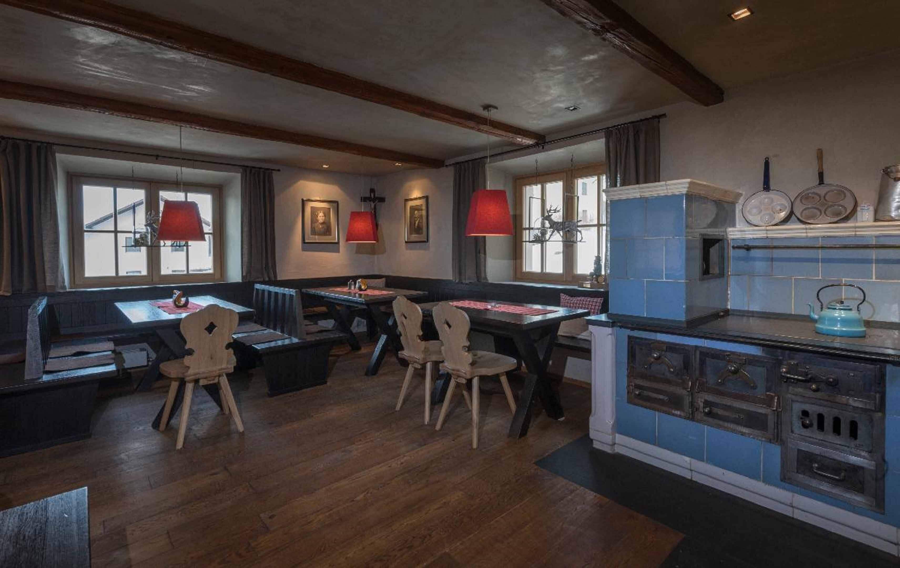 Een eetruimte met houten tafels en stoelen, een keuken met blauwe tegels en rode hanglampen.