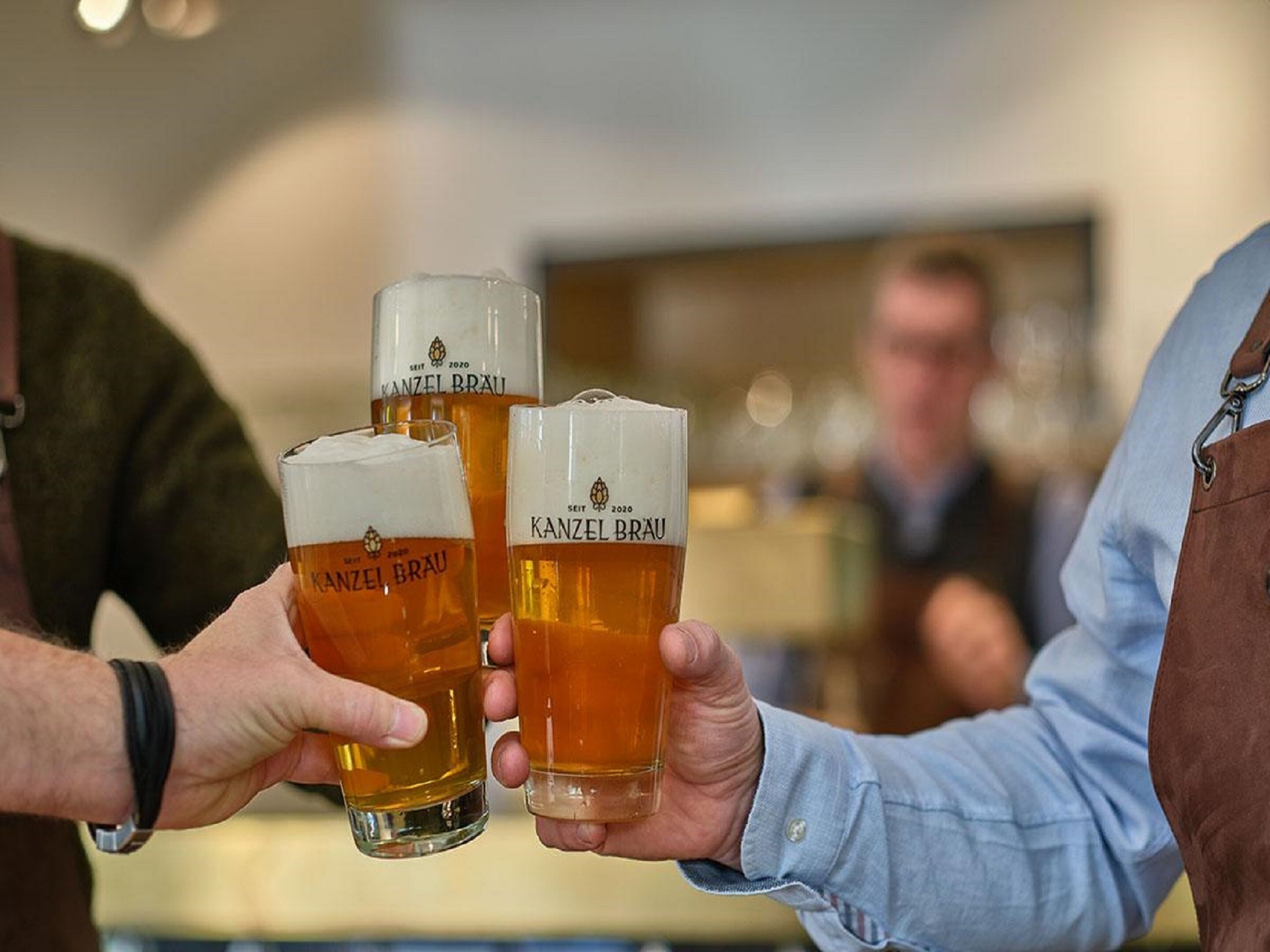 Zwei Personen halten Biergläser mit dem Aufdruck 'Kanzel Brau'.