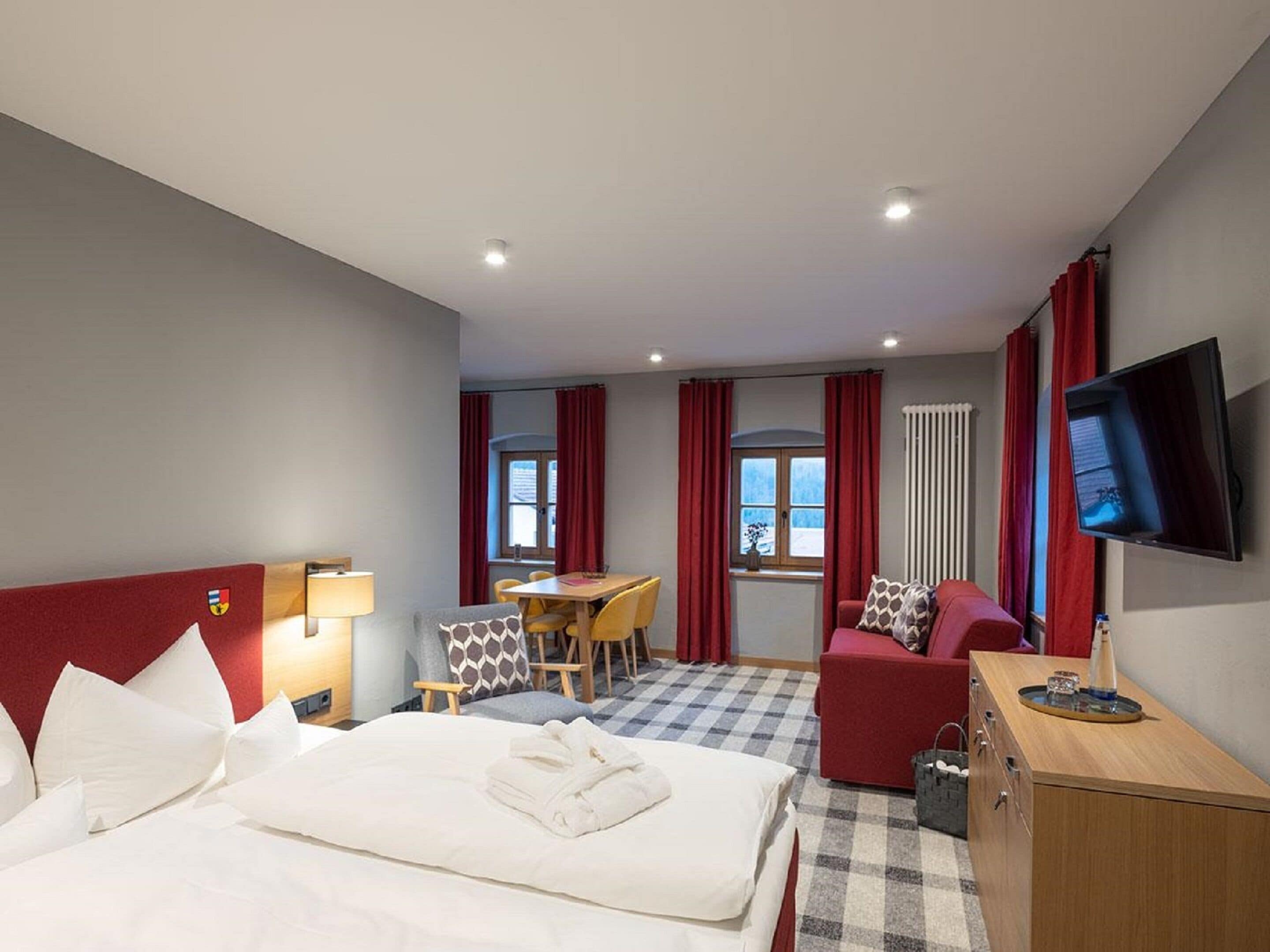 A hotel room with a bed, a desk, a sofa, a TV, and a window with curtains.