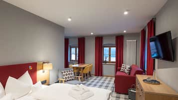 A hotel room with a bed, a desk, a sofa, a TV, and a window with curtains.