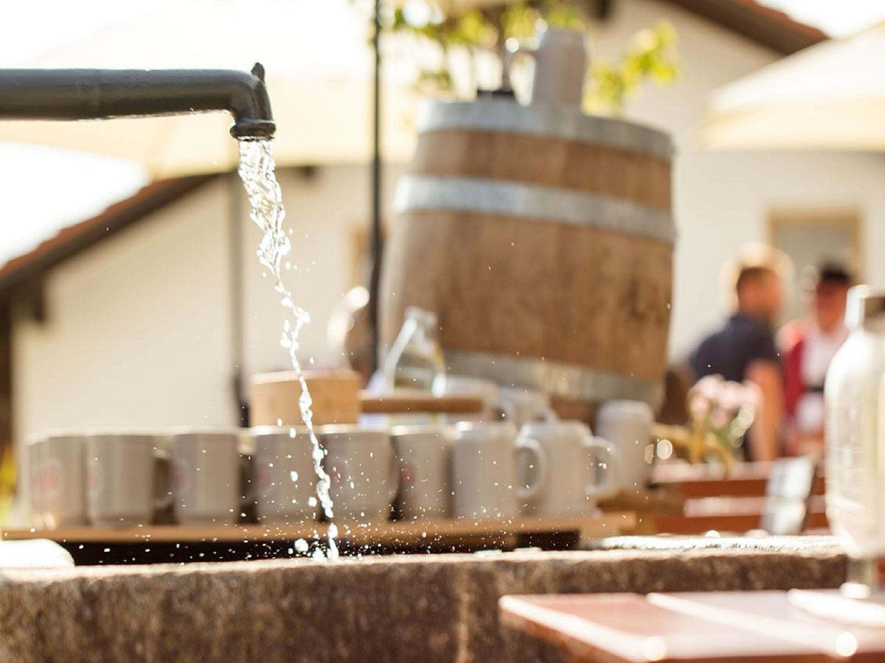 A water spout pouring water into a series of cups on a stone surface.