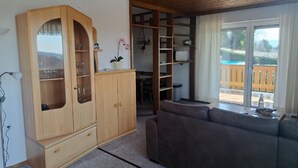 A cozy living room with a wooden cabinet, a sofa, and a sliding glass door leading to a deck. - Ferienwohnungen Alpenblick (Eppenschlag)