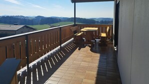 A balcony with a wooden railing, a table, and two chairs. - Ferienwohnungen Alpenblick (Eppenschlag)