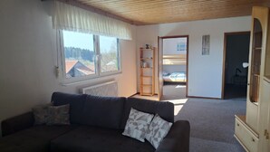 A cozy living room with a dark sofa, a wooden coffee table, and a window overlooking a rural landscape. - Ferienwohnungen Alpenblick (Eppenschlag)