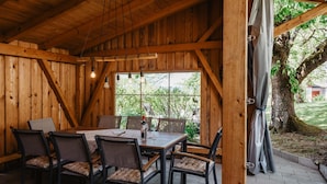 A wooden interior with a dining table and chairs, large windows, and a view of greenery outside. - Bio Ferienhof Winkler (Hutthurm)