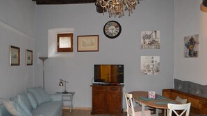 A living room with a sofa, TV, dining table, chairs, and a chandelier. - Appartamento in Centro (Spoleto)