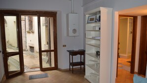 A room with a sliding glass door leading to a courtyard, a white radiator, and a white shelving unit with a small table. - Appartamento in Centro (Spoleto)