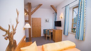 Een slaapkamer met een bed, een bureau, een stoel, een televisie en een raam met gordijnen.