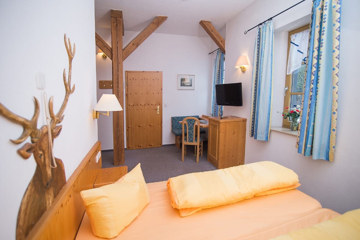 A bedroom with a bed, a desk, a chair, a television, and a window with curtains.