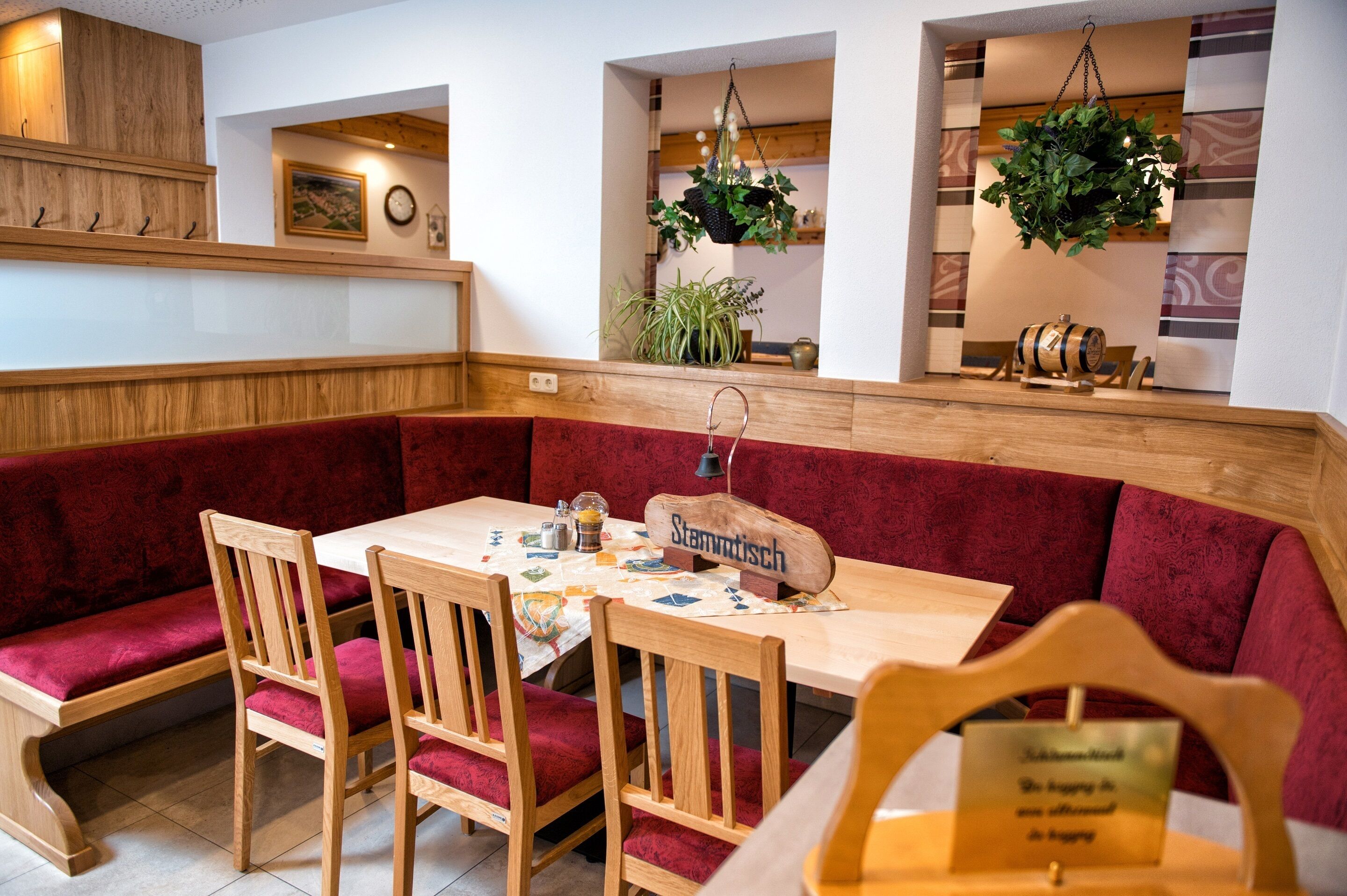 A cozy restaurant with wooden furniture, red cushioned seating, and hanging plants.