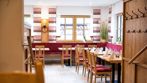 Een restaurant met houten meubels, een rode gewatteerde bank en grote ramen.