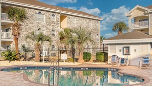 A pool area with a stone building, palm trees, and lounge chairs. - 4695 Wild Iris Drive, #204 Magnolia Place 2 Bedroom Condo by RedAwning (Myrtle Beach)
