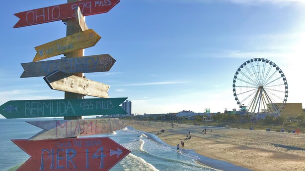 A beach with a signpost indicating distances to various locations. - 4695 Wild Iris Drive, #204 Magnolia Place 2 Bedroom Condo by RedAwning (Myrtle Beach)