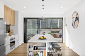 A modern kitchen with a central island, built-in appliances, and a sliding glass door leading to a patio. - Wye9 Beautiful Treetop And Beach Views Open (Wye River)