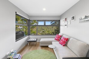 A modern living room with a large window, a sofa, a small table, and a green rug. - Wye9 Beautiful Treetop And Beach Views Open (Wye River)
