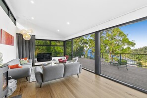 A modern living room with a large TV, grey sofas, and a wooden floor. - Wye9 Beautiful Treetop And Beach Views Open (Wye River)