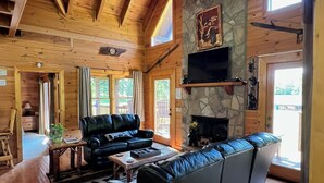 Un salón amplio con chimenea de piedra, vigas de madera en el techo y un sofá de cuero negro.