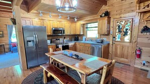 Interior de una cabaña de madera con cocina, comedor y un ventanal grande.