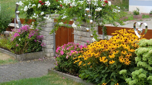 A garden with various flowers and a decorative metal structure. - Ferienwohnung Werner (Haundorf)