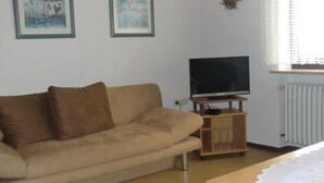 A living room with a beige sofa, a television on a wooden stand, and two framed pictures on the wall. - Ferienwohnung Werner (Haundorf)