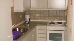 A compact kitchen with white cabinets, a stainless steel sink, a coffee maker, and a stove. - Ferienwohnung Werner (Haundorf)