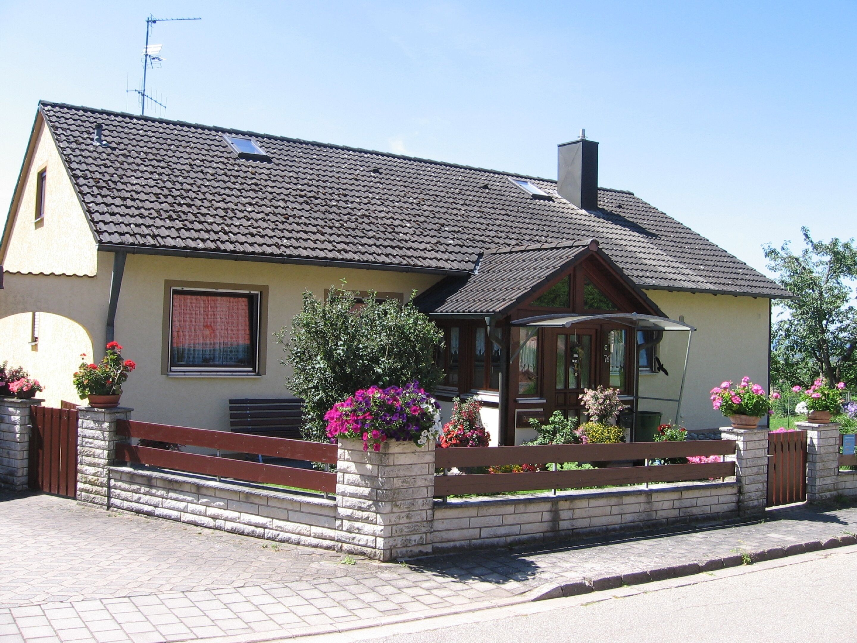 A two-story house with a tiled roof, a chimney, and a porch with a bench.