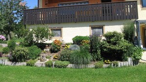 A two-story house with a balcony, surrounded by a well-maintained garden with various plants and flowers. - Ferienwohnung Werner (Haundorf)