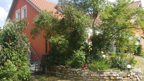 Una casa roja con un jardín de pared de piedra, una escalera y una silla.