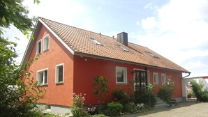 Una casa roja con techo de tejas, múltiples ventanas y un jardín con diversas plantas y flores.