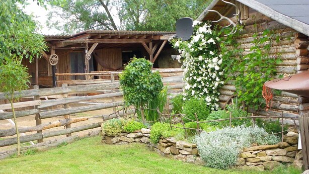 Una cabaña rústica de troncos con un muro de piedra y una valla de madera.