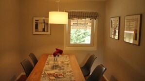 A dining area with a wooden table, chairs, a vase with red flowers, a hanging light fixture, and framed pictures on the walls. - Tauberlodge (Creglingen)