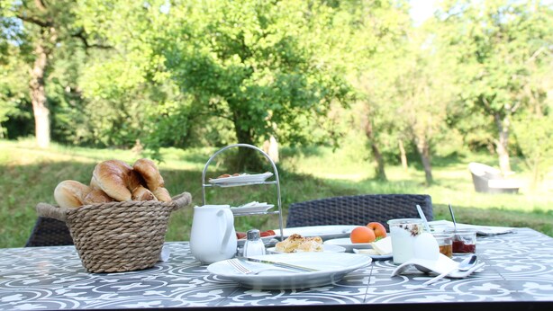 An outdoor dining table with a basket of bread, a tea set, and a plate of food. - Tauberlodge (Creglingen)