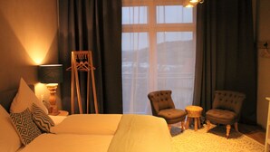 A bedroom with a large bed, two armchairs, a small table, and a window with curtains. - Tauberlodge (Creglingen)
